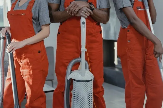Three people in a uniform with cleaning appliances - cleaning business concept