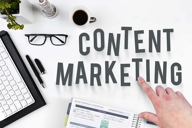 Hand pointing to the words content marketing on a table with a notebook and keyboard